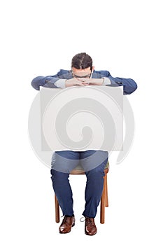 Overwhelmed businessman seated on chair leaning head on a big blank banner with copy space for messages. Full length exhausted