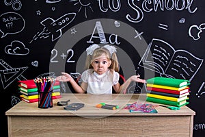 Overwhelmed disappointed schoolgirl sitting at the desk with books, school supplies, holding her both arms with palms