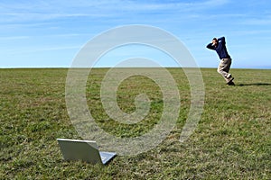 Overwhelmed man running in field away from laptop