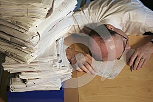 Un hombre de negocios pone su cabeza sobre la mesa con el cansancio como él se siente abrumado por una pila de papeles.