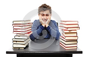 Overwhelmed student with face in hands sitting at his desk between two piles of books