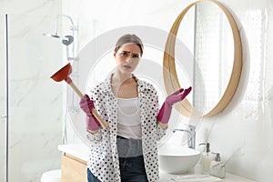 Overwhelmed woman with plunger near sink in bathroom