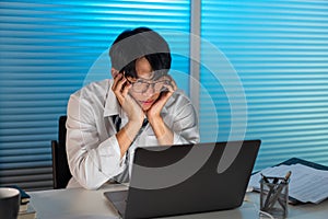 Overwork Concept The man in the office resting his face on his hands and staring at the laptop screen photo