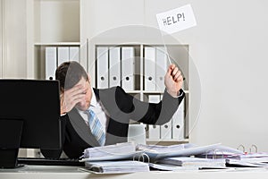 Overworked Accountant Holding Help Sign At Desk