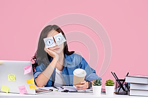 Overworked Asian women. She was sitting at her desk with stickers covering her eyes and using her laptop on a pastel pink