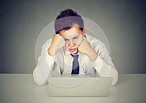 Overworked bored man sitting at desk with laptop computer looking down