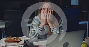 Overworked female employee working in empty office late at night with her laptop. Exhausted young woman looking tired