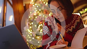 overworked female freelancer working in xmass decorated coffee shop on Christmas Eve using phone, laptop and notebook