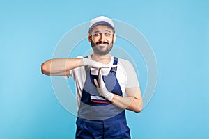 Overworked handyman in overalls and gloves showing time out gesture, need break. Profession of service industry