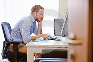 Overworked Male Doctor In Office Sitting At Computer