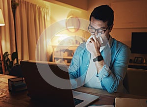 Overworked man blowing his nose while working on laptop at home