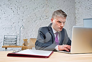 Overworked mature businessman looking at laptop on desk in office