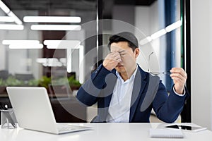 Overworked and overtired man has severe dizziness in head, businessman rubs eyes, eye pain long work at laptop, asian photo