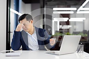 Overworked and overtired man has severe dizziness in head, businessman rubs eyes, eye pain long work at laptop, asian photo