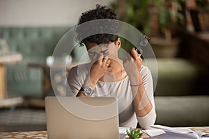 Overworked tired african woman holding glasses feel eye strain