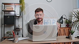 Overworked tired freelance businessman working on laptop showing inscription notebook with Help text