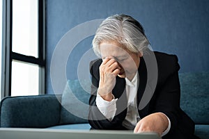 Overworked tired old lady holding head feeling headache. Asian senior business woman stress from hard work. Frustrated business