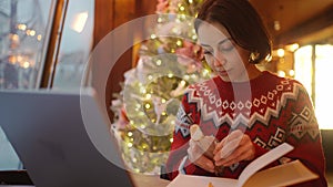 overworked woman freelancer working in xmass decorated coffee shop on Christmas Eve using laptop and notebook. remote