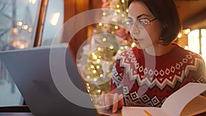 overworked woman freelancer working in xmass decorated coffee shop on Christmas Eve using laptop and notebook. remote