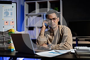 Overworked young Asian office employee working on laptop computer overtime in office at night