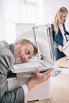 overworked young businessman sleeping with head on copier