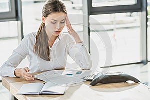 overworked young businesswoman with headache doing paperwork