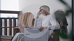 Overworked young Chinese man sitting on deck in the evening with laptop and graph. Side view of tired exhausted Asian