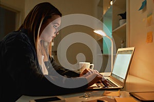 Overworking. Side view of young caucasian woman working from home in dark late night, using laptop and drinking coffee