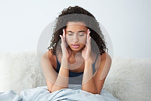 Ow, is that a headache. an attractive young woman suffering from a headache and rubbing her head while in bed.