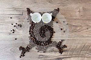 Owl shaped figure made out of coffee beans and two empty espresso cups on top of a table