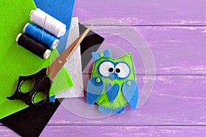 Owl toy is sewn from plush felt. Green fabric owl with blue heart and bow. Home decor idea for beginners and children