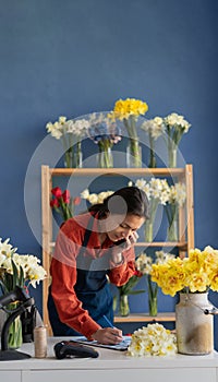 Own business concept. Businesswoman talking on mobile phone while standing in small floral shop and writing order