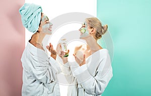 Own spa salon at home. Conception of skin care by using white mask and cucumbers on the face. Two female sisters have