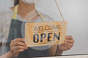 Owner business retail, asian young woman hand in turning sign board to open coffee shop, wearing face mask protect to pandemic of