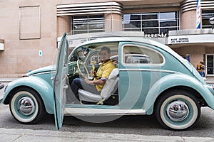 Owner of classic Volkswagen pale blue Beetle sitting in his car proudly holding golden trophy