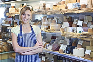 Owner Of Delicatessen Standing Next To Cheese Display