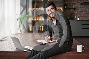 owner of a new business is taking notes in a notebook while sitting on the floor.