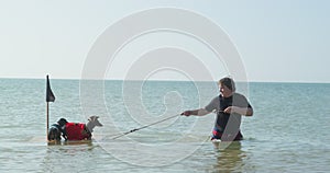 Owner is playing with his pets. Man in sea drags raft tied to a rope, on which two funny dachshund dogs in privateer