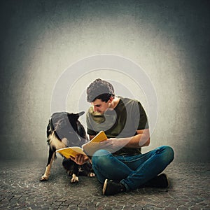Owner seated on floor training his cute puppy reading together an interesting book
