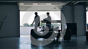 Owners of a racing car are observing it in the workshop