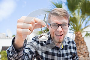 Ownership, real estate, property and tenant concept - Portrait of a cheerful young man holding key from new home