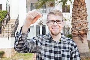 Ownership, real estate, property and tenant concept - Portrait of a cheerful young man holding key from new home