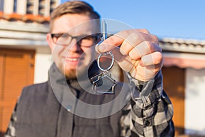 Ownership, real estate, property and tenant concept - Portrait of a cheerful young man holding key from new home