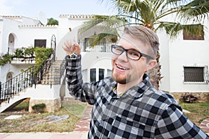 Ownership, real estate, property and tenant concept - Portrait of a cheerful young man holding key from new home