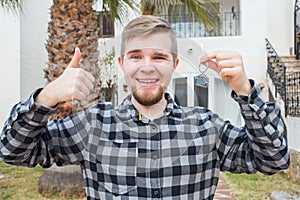 Ownership, real estate, property and tenant concept - Portrait of a cheerful young man holding key from new home