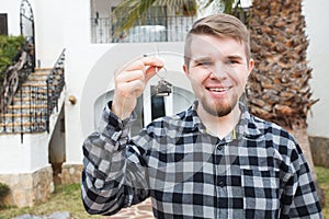 Ownership, real estate, property and tenant concept - Portrait of a cheerful young man holding key from new home