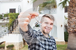 Ownership, real estate, property and tenant concept - Portrait of a cheerful young man holding key from new home