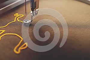 An ox symbol is stitched by an embroidery machine on shiny olive green fabric with golden yarn in bright luxury light