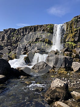 Oxararfoss waterfall against a blue sky flowing down the rocks at Thingvellir National Park