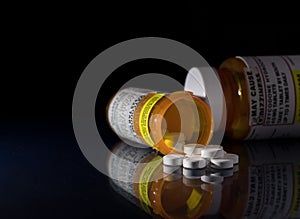 Macro of oxycodone opioid tablets with prescription bottles against dark background